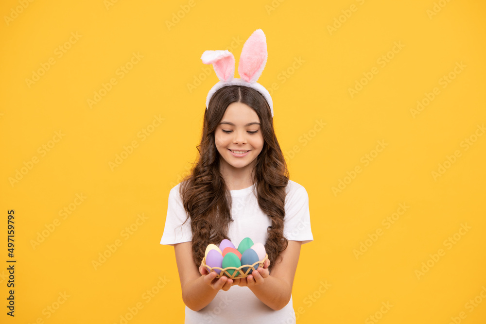 smiling child in bunny ears hold eggs on yellow background, easter