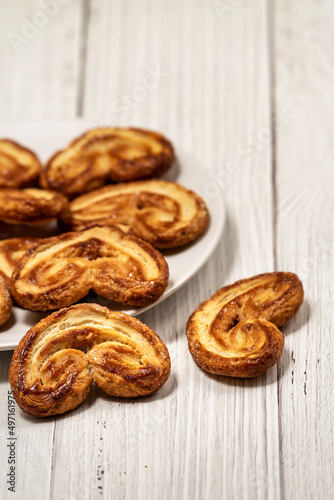  Palmier puff pastry biscuits in white plate on a white painted wooden table