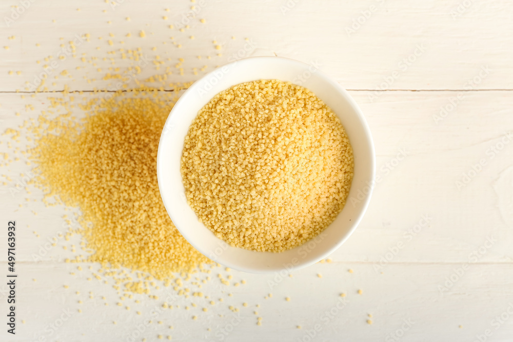 Bowl of raw couscous on white wooden background