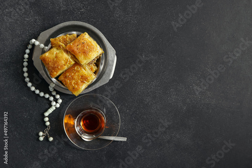 Tasty Turkish baklava with tasbih and tea on dark background
