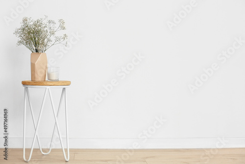 Beige vase with gypsophila flowers and candle on table near light wall