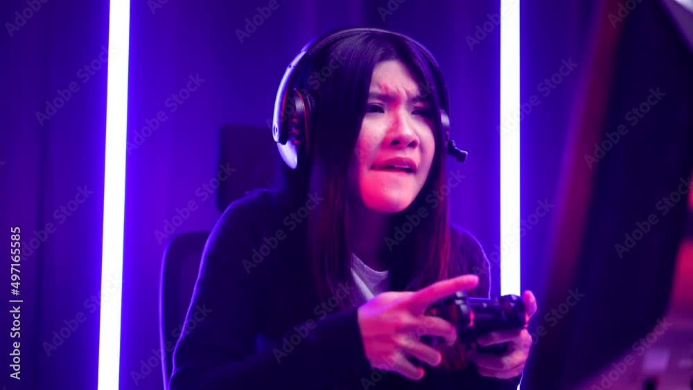 Gamer with controller losing moment. Young asian pretty woman sitting on chair with computer pc. Female Professional Streamer wearing headphone playing game online in dark room neon light. Gamer with controller losing moment. Young asian pretty woman sitting on chair with computer pc. Female Professional Streamer wearing headphone playing game online in dark room neon light.