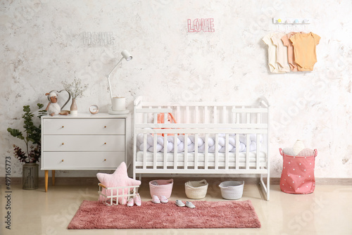 Interior of light children's bedroom with crib and baby bodysuits photo
