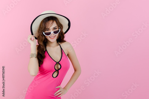Portrait of happy asian young woman wear pink summer dress brim hat and sunglass looking at camera standing pink background. studio shot. fashion lifestyle concept.