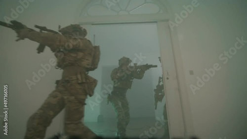 Group of men in camouflage uniform playing airsoft indoor. Front view of men entering dark room, moving forward together, covering and defending each other in building. Attack, airsoft game concept photo