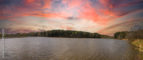 a panoramic shot of a vast rippling lake surrounded by lush green trees with powerful red clouds at sunset at Murphey Candler Park in Atlanta Georgia USA photo
