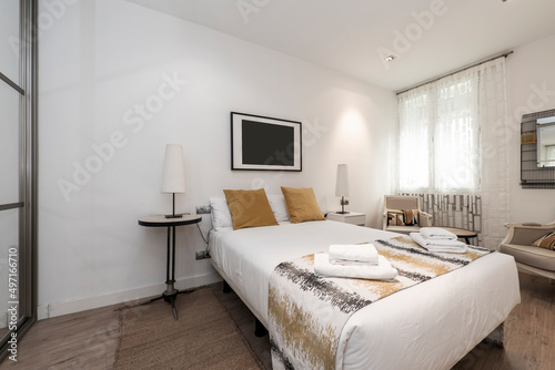 Bedroom with a large double bed with gold cushions  mismatched side tables  towels on the bed  and a wardrobe with mirrored sliding doors