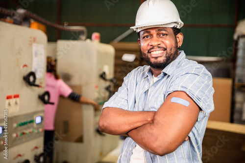 African workers  pointing at his arm with a bandage after receiving the covid-19 vaccine.Vaccination for Essential Workers in healthcare at industrial factory.