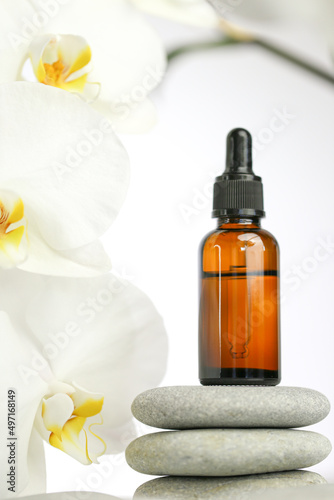 Beauty and aromatherapy.Massage oil and massage stones. bottle with oil on gray stones and white orchid flower on white background.Spa and relaxation.White orchid flower  massage stones and oil 