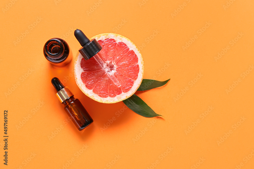 Bottles with essential oil and half of grapefruit on color background Bottles with essential oil and half of grapefruit on color background