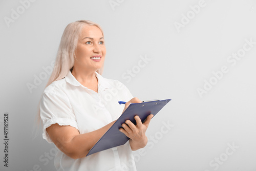 Mature secretary with clipboard on light background