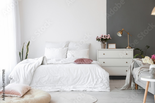 Comfortable bed, chest of drawers and sofa in stylish room interior