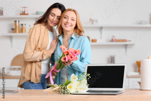 Laptop and bouquet of flowers on table in kitchen