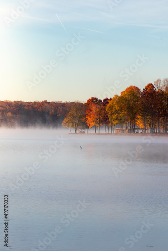 View of Blue Skies Along Foggy Lake with Trees with Fall Foliage  © suraju