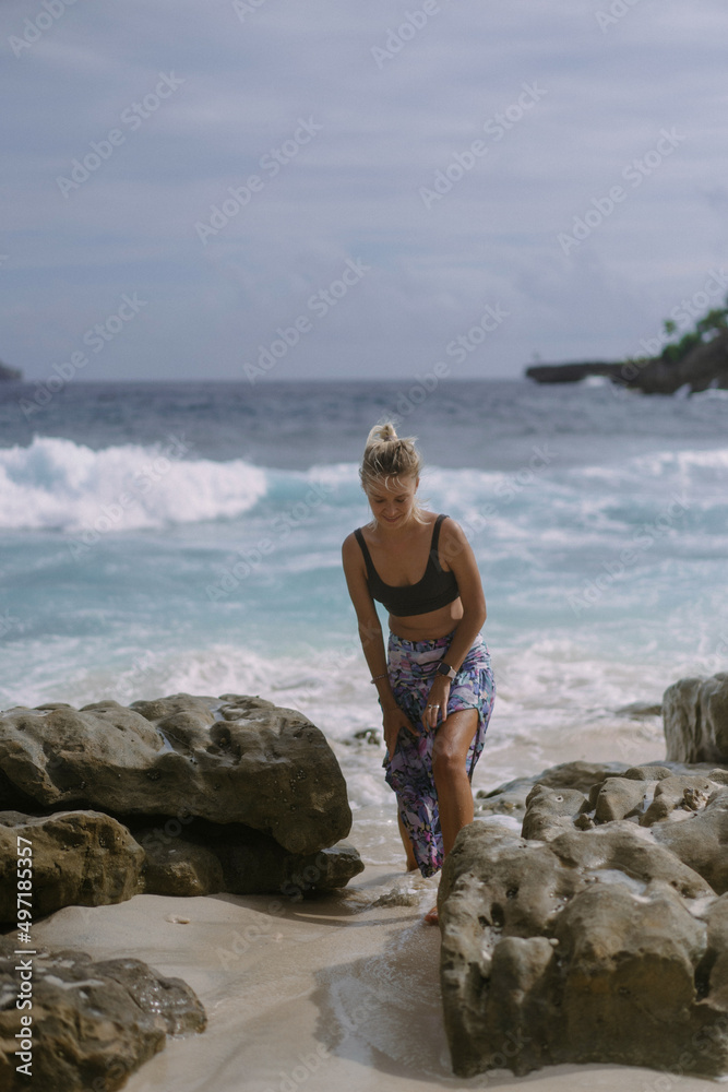 Young woman on a journey. Traveler on a rock by the ocean.