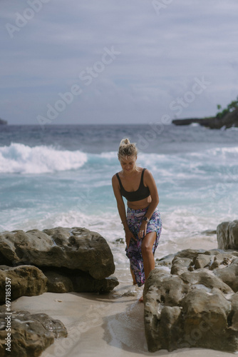 Young woman on a journey. Traveler on a rock by the ocean.
