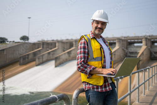 Fotografie Portrait of engineer wearing yellow vest and white helmet with laptop computer Working day on a water dam with a hydroelectric power plant