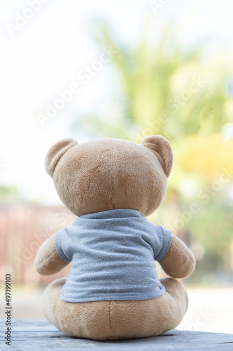 Vertical photo Brown teddy bear facing the camera sitting on a wooden background with green tone background.