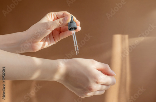 Concept of rejuvenation, body care. Pipette with cosmetic serum in women's hands in rays of sunlight. photo