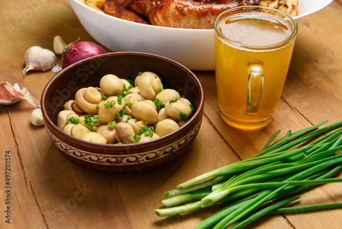 fried chicken meat and roasted potatoes on a white platter, a glass of beer, champignon mushrooms and green onions, delicious food on a wooden background