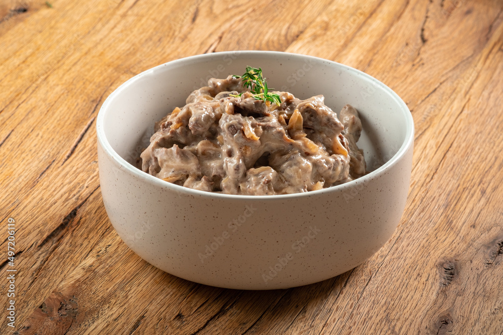 Beef in cream sauce with mushrooms and onions in a bowl on a wooden table. A dish of beef stroganoff served on the table Beef in cream sauce with mushrooms and onions in a bowl on a wooden table. A dish of beef stroganoff served on the table