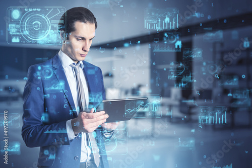 Attractive european businessman using tablet with abstract creative business charts and binary code on blurry office interior background. System engineering and digital transformation concept. 