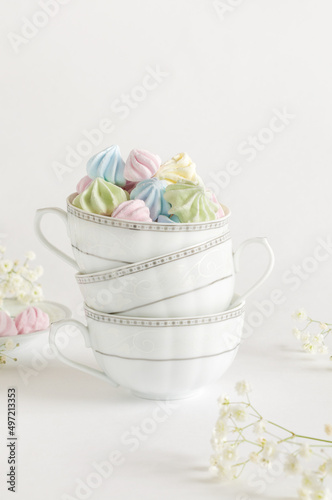 Colored airy meringues on a gray background in tea mugs. Vertical image, selective focus