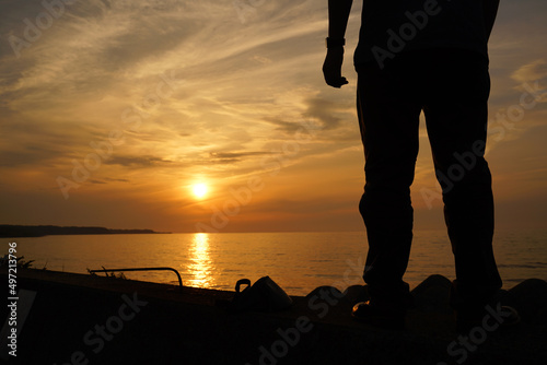 防波堤に立って海に沈む夕日を見ている男性 