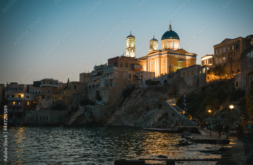 Church of Saint Nicholas, a magnificent church in Ermoupolis, the capital of Syros island. Vaporia district of Ermoupoli town, Syros Island. Landscape with buildings along the coastline at sunset
