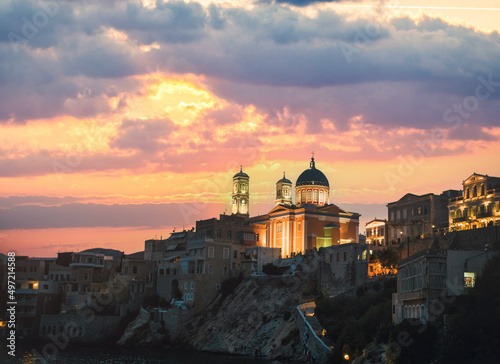 Church of Saint Nicholas, a magnificent church in Ermoupolis, the capital of Syros island. Vaporia district of Ermoupoli town, Syros Island. Landscape with buildings along the coastline at sunset