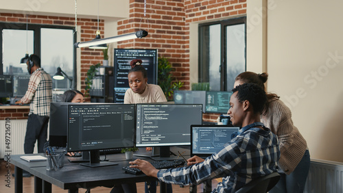 Programmer analyzing compiling code on multiple screens takes off glasses and doing high five hand gesture with colleague developer. Software developers celebrating successful coding.
