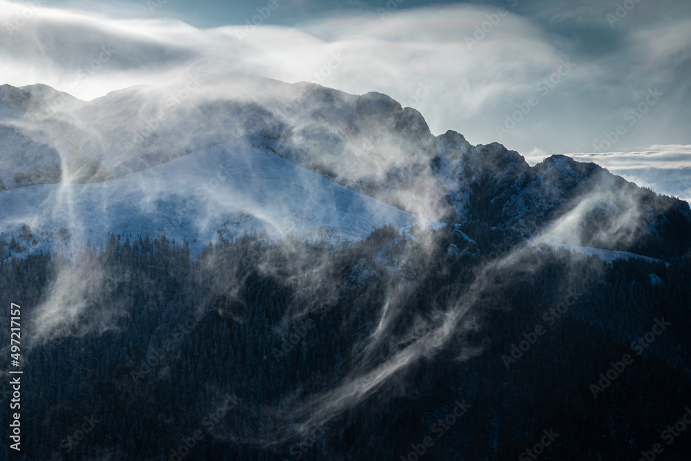 Snow blizzard on top of the mountains creating vortex clouds. Freezing winter landscape.