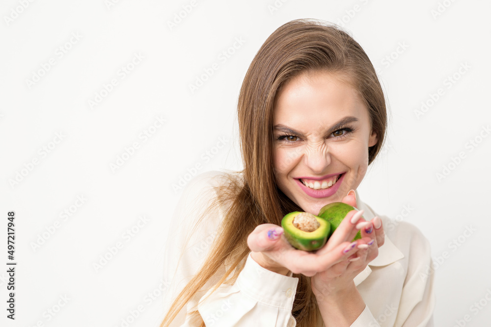 Portrait of a lovely smiling young brunette caucasian woman wearing the white shirt with long hair holding and showing avocado, standing isolated over white background Portrait of a lovely smiling young brunette caucasian woman wearing the white shirt with long hair holding and showing avocado, standing isolated over white background