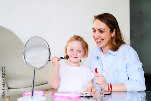 Young happy mom playing with her preschool daughter and doing makeup