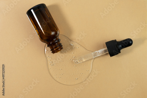 Serum, gel, essential oil, lotion or hyaluronic acid is poured from a bottle of dark amber glass with a pipette on a beige background. Wellness and beauty concept.