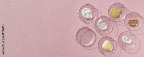 Multicolored texture of cream, scrub, serum, oil and hyaluronic acid in Petri dishes on a pink background. Concept of cosmetics laboratory researches. Smear of skincare cosmetics product. Banner