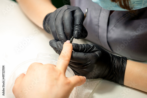 Close up professional manicurist master holding customer hand while using a cuticle pusher in a nail salon © okskukuruza
