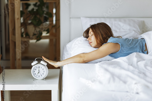 Woman sleep on the bed turns off the alarm clock wake up at the morning, Selective focus.Young woman reaching to turn off alarm clock ,early morning