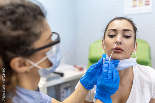 Medical worker wearing personal protective equipment doing corona virus swab on female patient - Covid19 test and health care concept