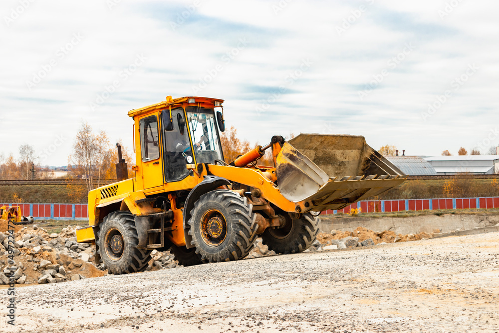 The loader is transporting sand or gravel in the front bucket. Heavy construction equipment at a construction site. Transportation of bulk materials in a concrete plant. The loader is transporting sand or gravel in the front bucket. Heavy construction equipment at a construction site. Transportation of bulk materials in a concrete plant.
