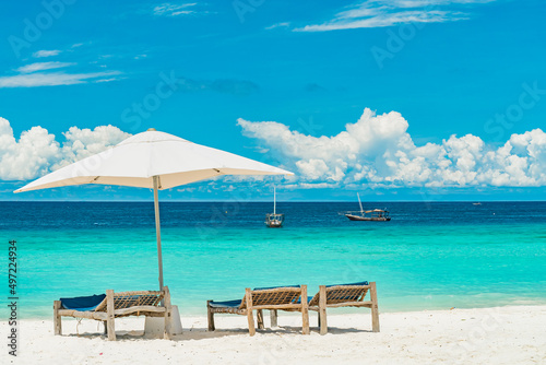 Fototapeta Naklejka Na Ścianę i Meble -  Wooden deck chairs on a sandy beach in front of ocean with boats, Zanzibar Tanzania