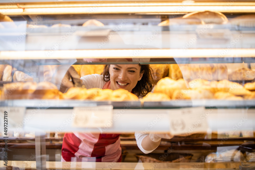 Bakery seller arranging freshly baked pastry products on shelf in bakery shop.