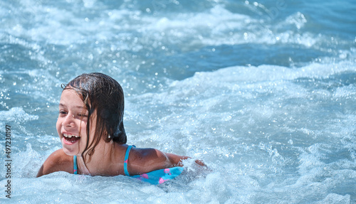 Banner. Joyful child swims in sea. Young girl is covered by wave, smiles, rejoices, bathes, swims, splashes in sea waves.