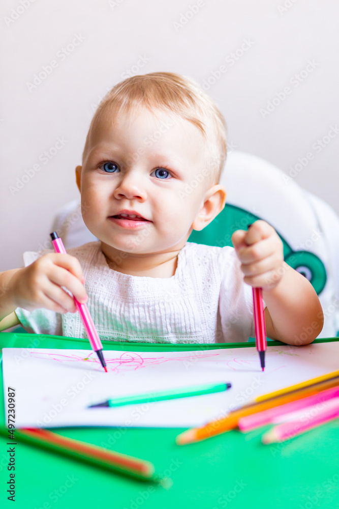 cute little artist draws in an album with pencils, sitting at a small table.