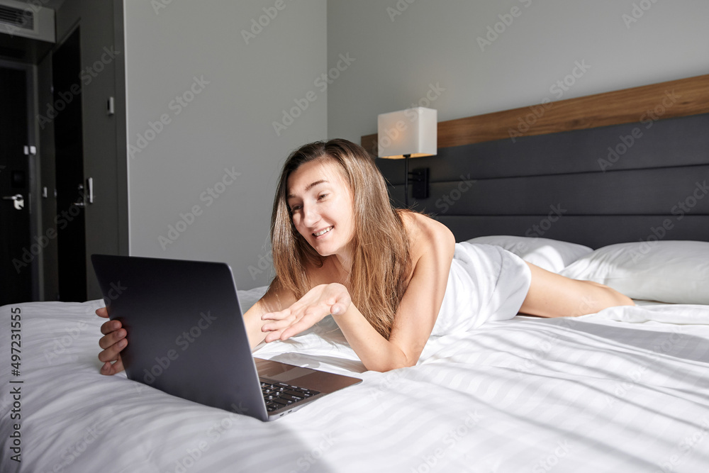 A young pretty woman lies in a white towel in front of her laptop and points her finger at it. A girl with a laptop on the bed points her finger at the screen. Works at the hotel's laptop. A young pretty woman lies in a white towel in front of her laptop and points her finger at it. A girl with a laptop on the bed points her finger at the screen. Works at the hotel's laptop.