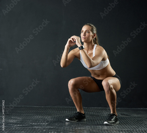 The perfect squat. Studio shot of an attractive young woman doing squats against a dark background.
