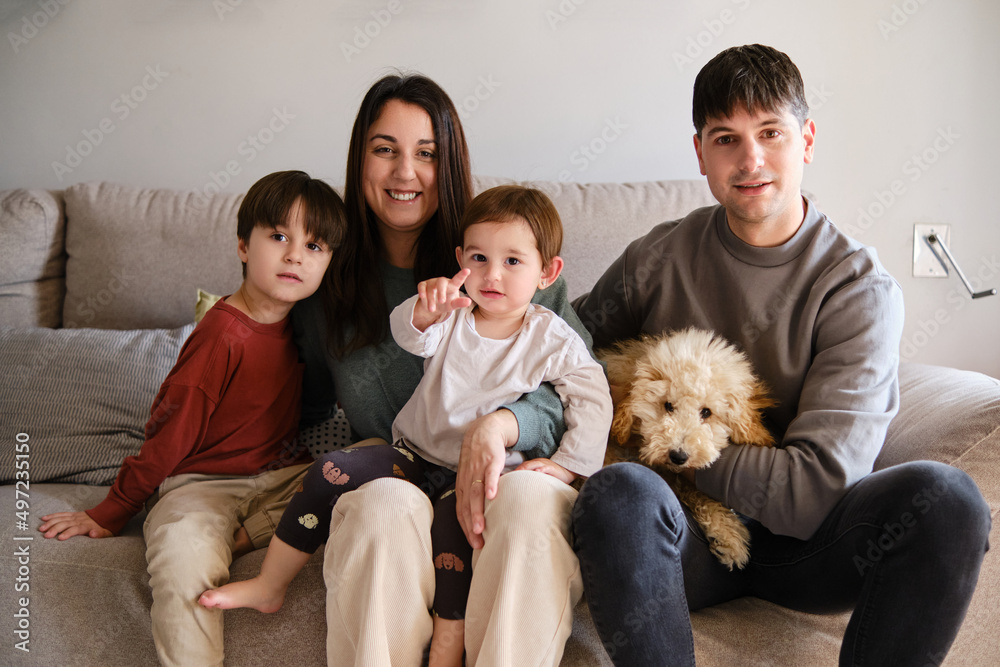 Portrait of a family sitting together with their dog on the sofa in the living room at home. Portrait of a family sitting together with their dog on the sofa in the living room at home.