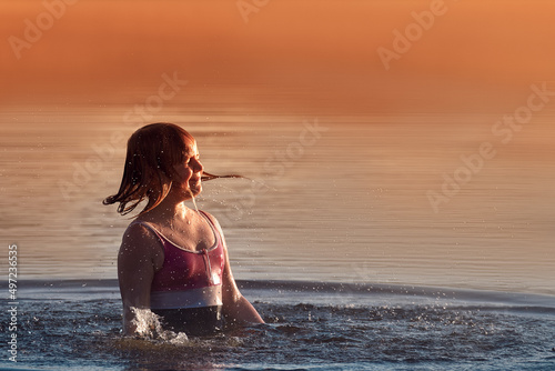 Happy girl 10-11 years old splashes water in the sea in summer. A cheerful child swims and plays in the water at sunset.