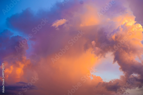 Big bright colorful thunder cloud at grave sunset. Yellow, orange, lilac thundercloud with rain illuminated by the sun