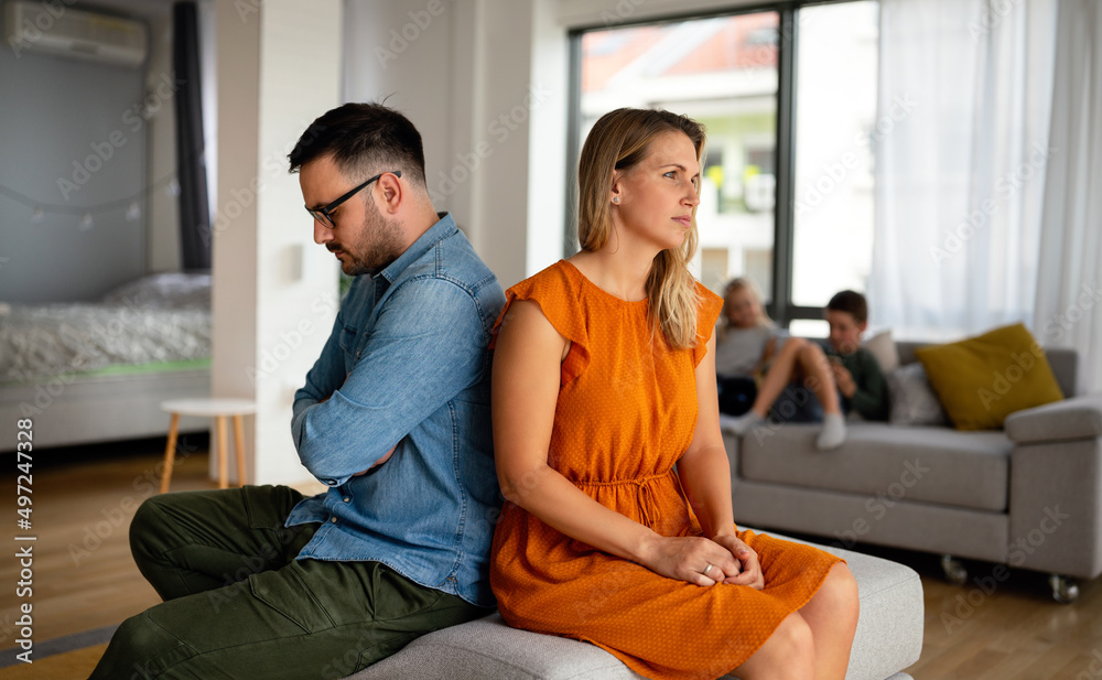 Sad pensive couple thinking of relationships problems sitting on sofa, conflicts in marriage.